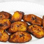 The fried plantains arranged on a white plate with parsley as a garnish on the left side.