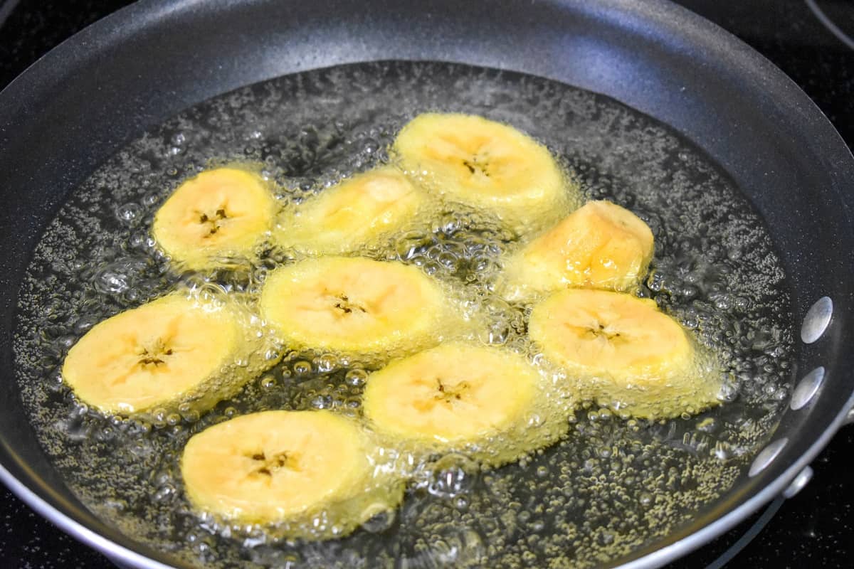 Nine slices cooking in a black skillet, the oil is bubbling around them.