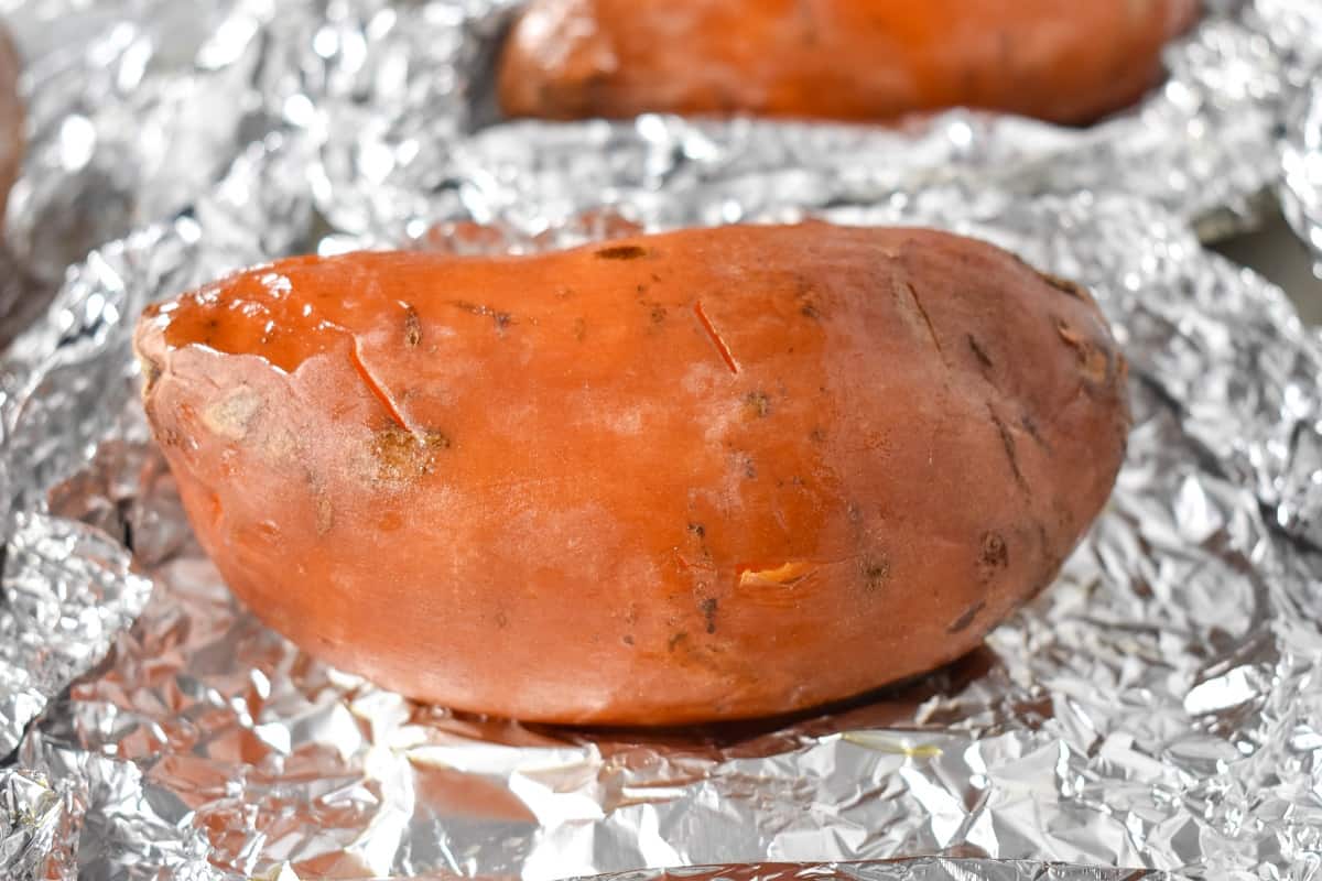 A baked sweet potato sitting on the foil it was wrapped in.