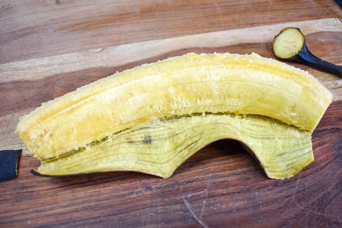 A half peeled ripe plantain on a wood cutting board.