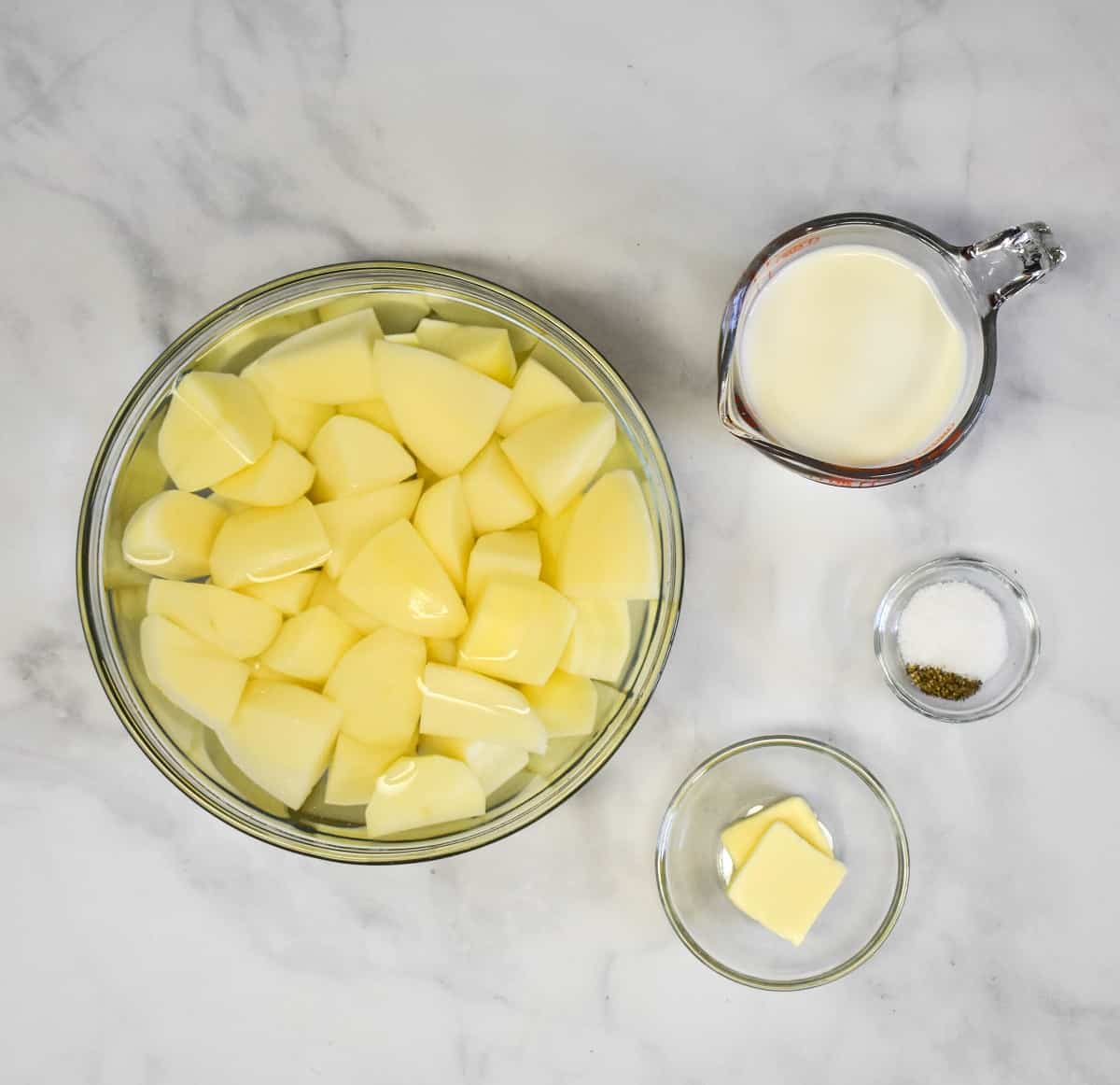 The ingredients for the mashed potatoes prepped and arranged on a white table.