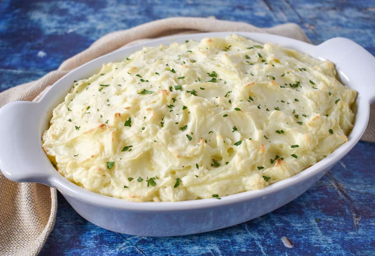 The finished turkey shepherd's pie in a white casserole displayed on a blue table with a beige linen in the background.