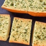 Homemade garlic bread cut into pieces and arranged on a black cutting board.