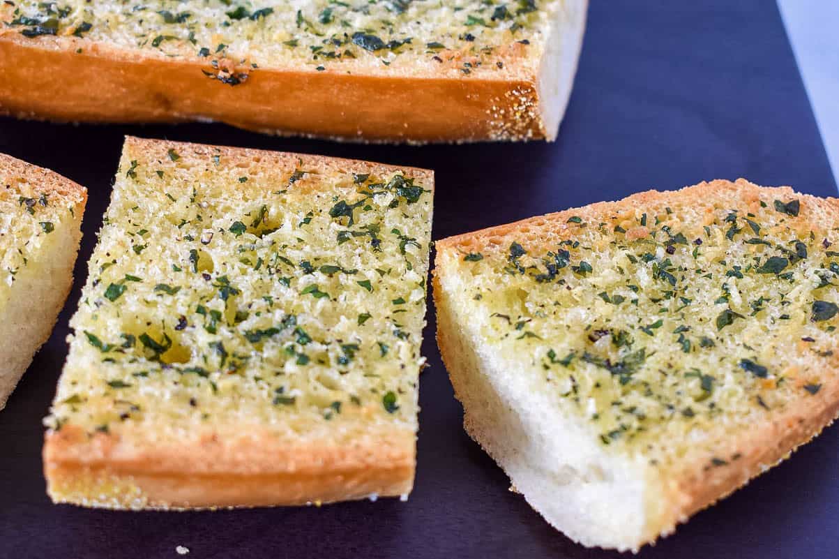A close up of sliced garlic bread on a dark cutting board.