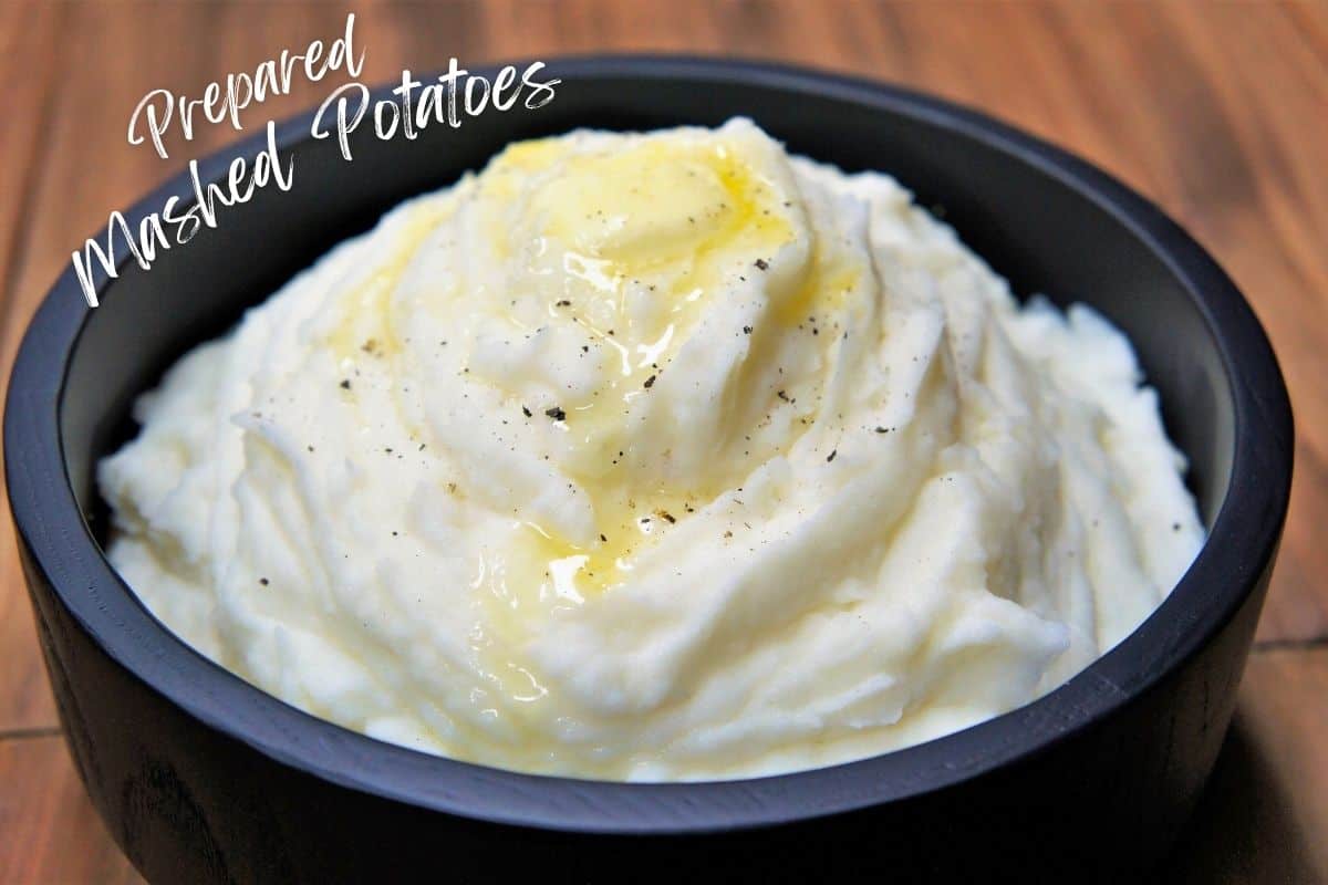 Bowl of creamy prepared mashed potatoes topped with melted butter and cracked black pepper.