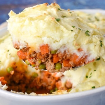 A serving spoon lifting a serving of shepherd's pie out of a white casserole dish.