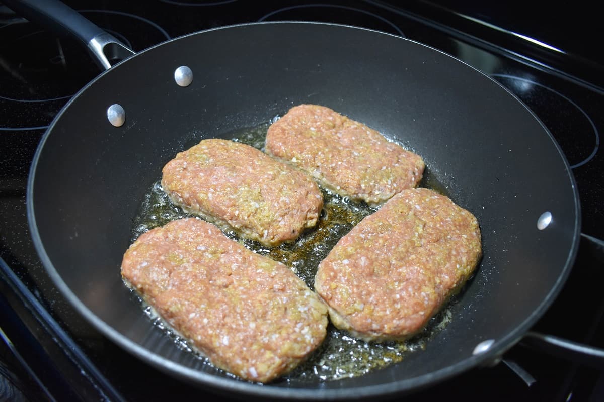 Four patties browning in a large black skillet.