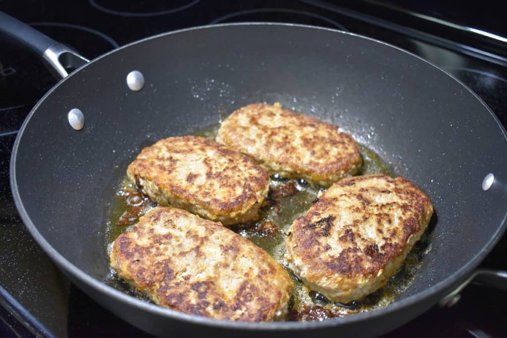 Four patties in a large, black skillet after being flipped so the top side is browned.