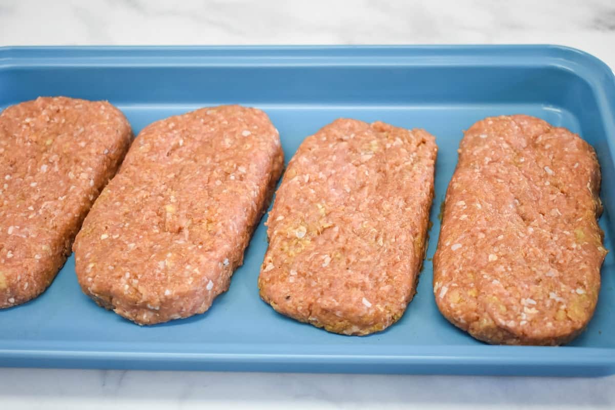 Four formed Salisbury steak patties arranged on a light blue tray.