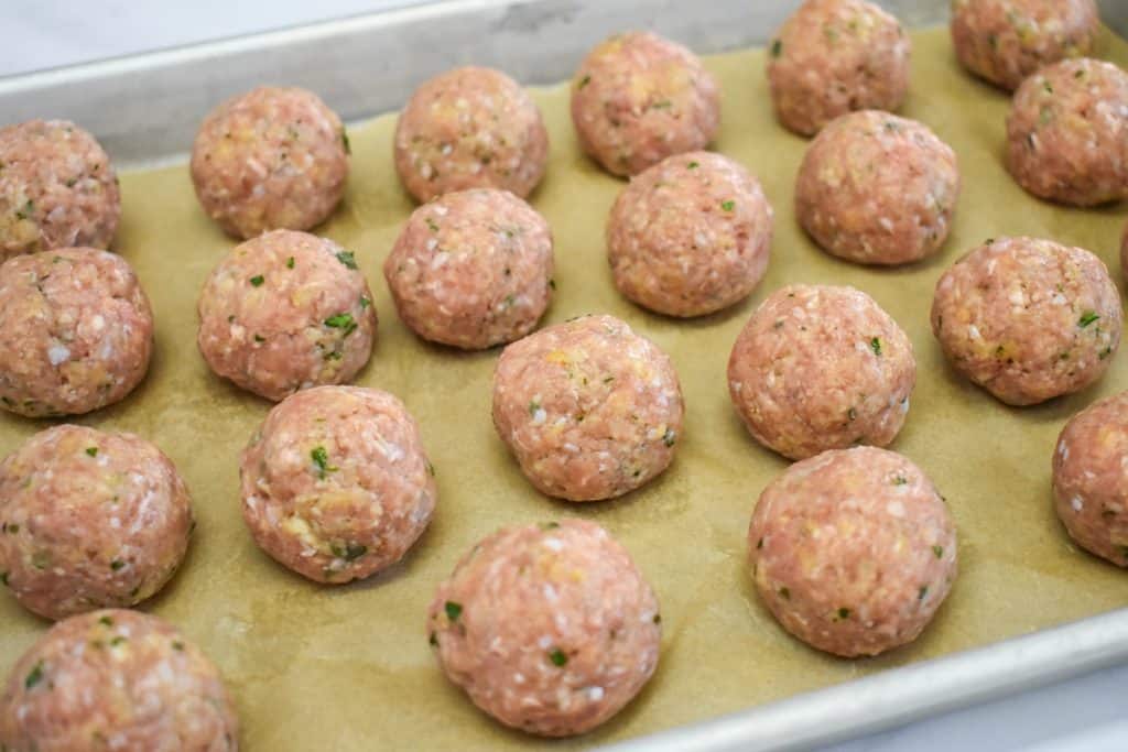 The formed meatballs set on a parchment paper lined baking sheet.