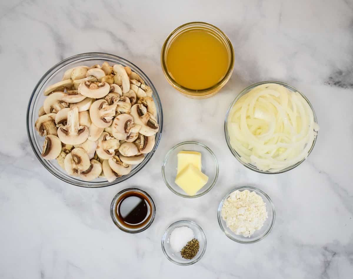 The ingredients for the mushroom gravy separated in glass bowls and displayed on a white table.