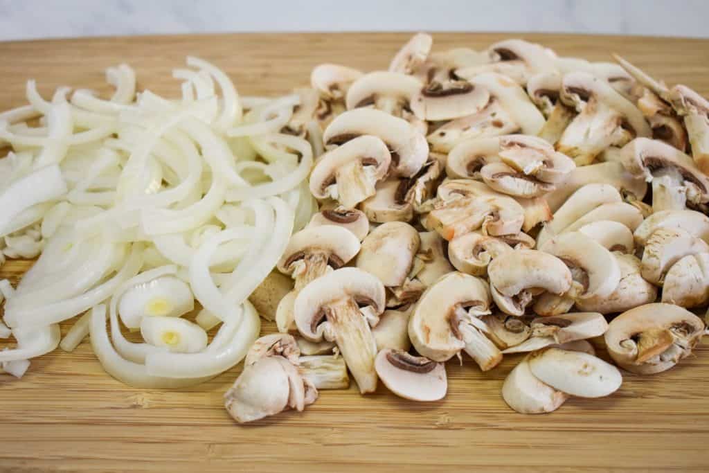 Sliced onions and mushrooms on a wood cutting board.