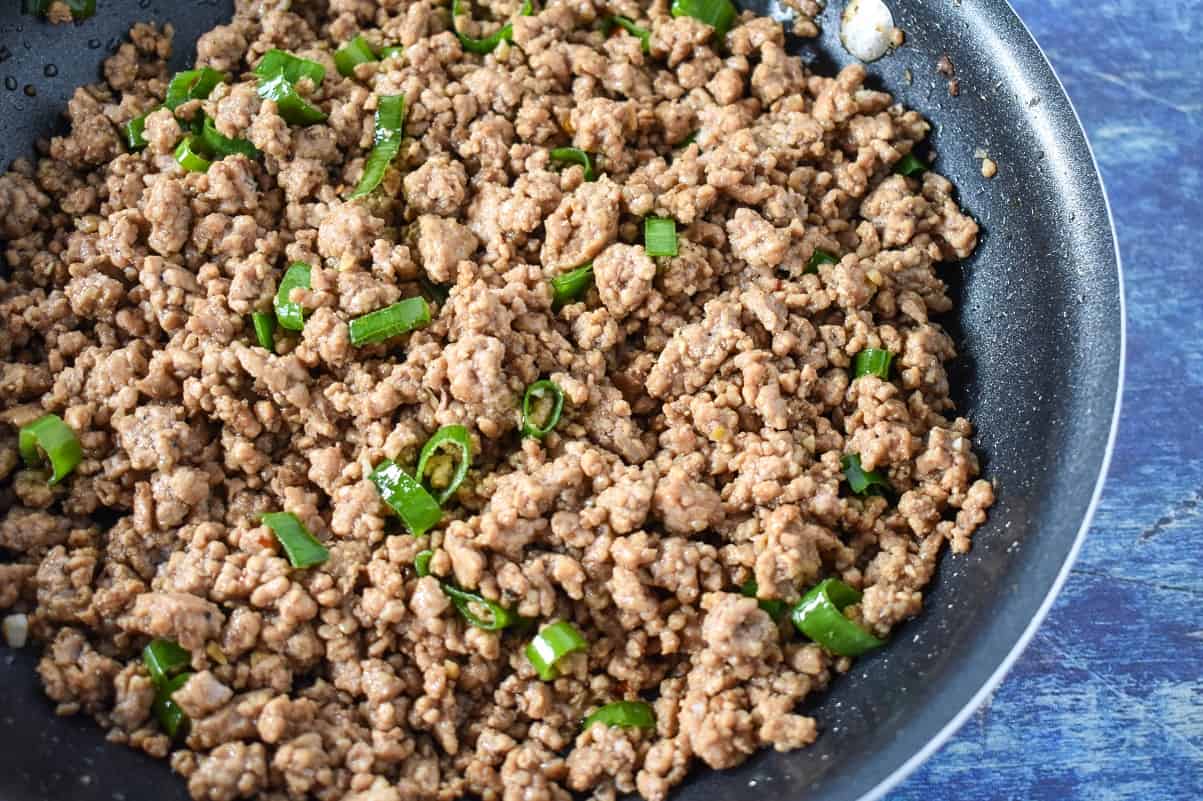 The cooked pork filling with green onions, still in the skillet and displayed on a blue table.