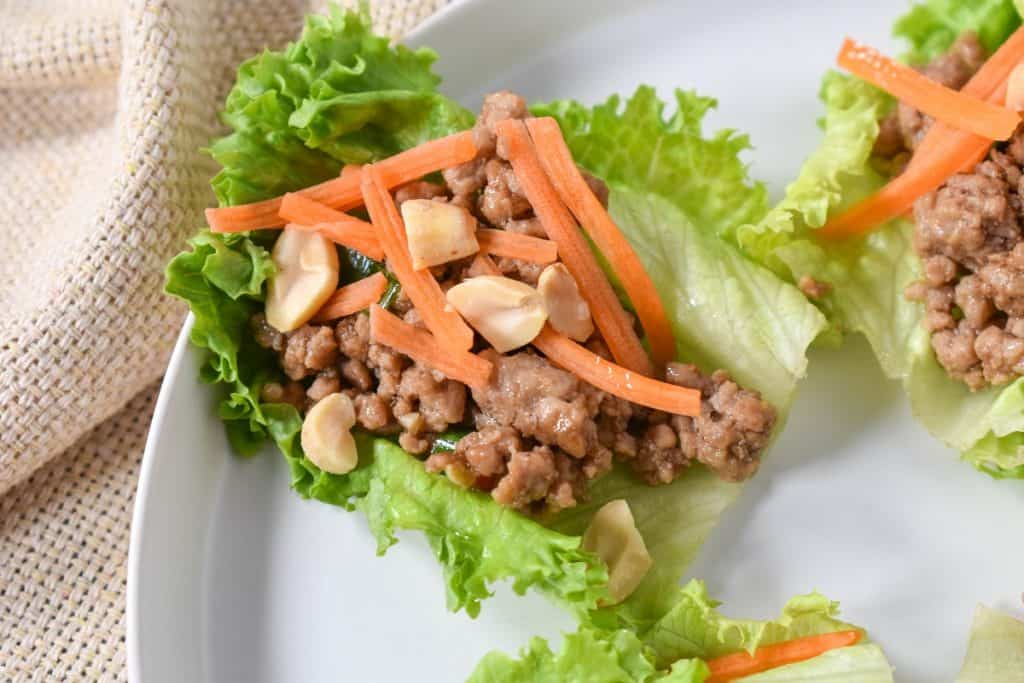 A pork lettuce wrap garnished with shredded carrots and peanuts, served on a white plate.