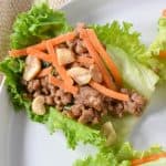 A pork lettuce wrap garnished with shredded carrots and peanuts, served on a white plate.