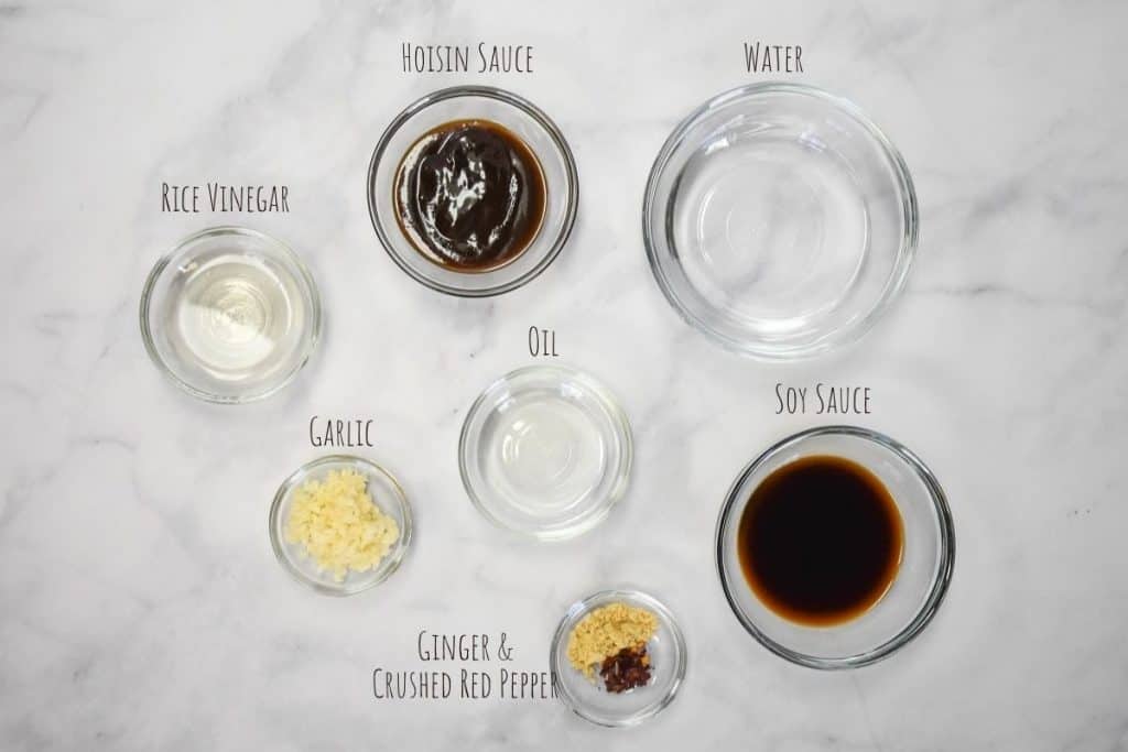 The ingredients for the Asian sauce arranged in small bowls on a white table with the label of each ingredient written on top of the bowl.