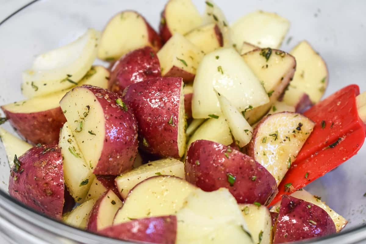 The potatoes and onions mixed with the seasoning in a large glass bowl.