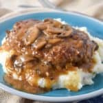 The finished dish served on a bed of mashed potatoes on a blue plate with a beige linen.