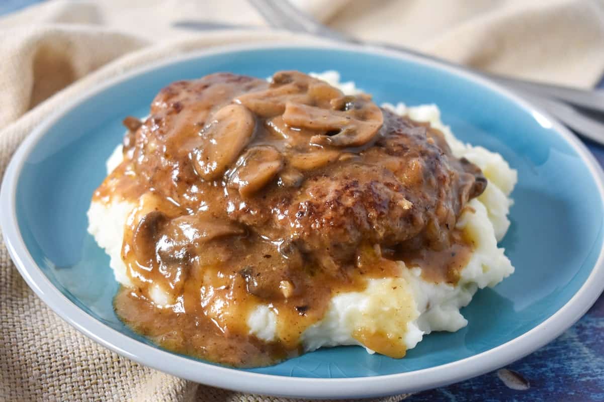 The finished dish served on a bed of mashed potatoes on a blue plate with a beige linen.