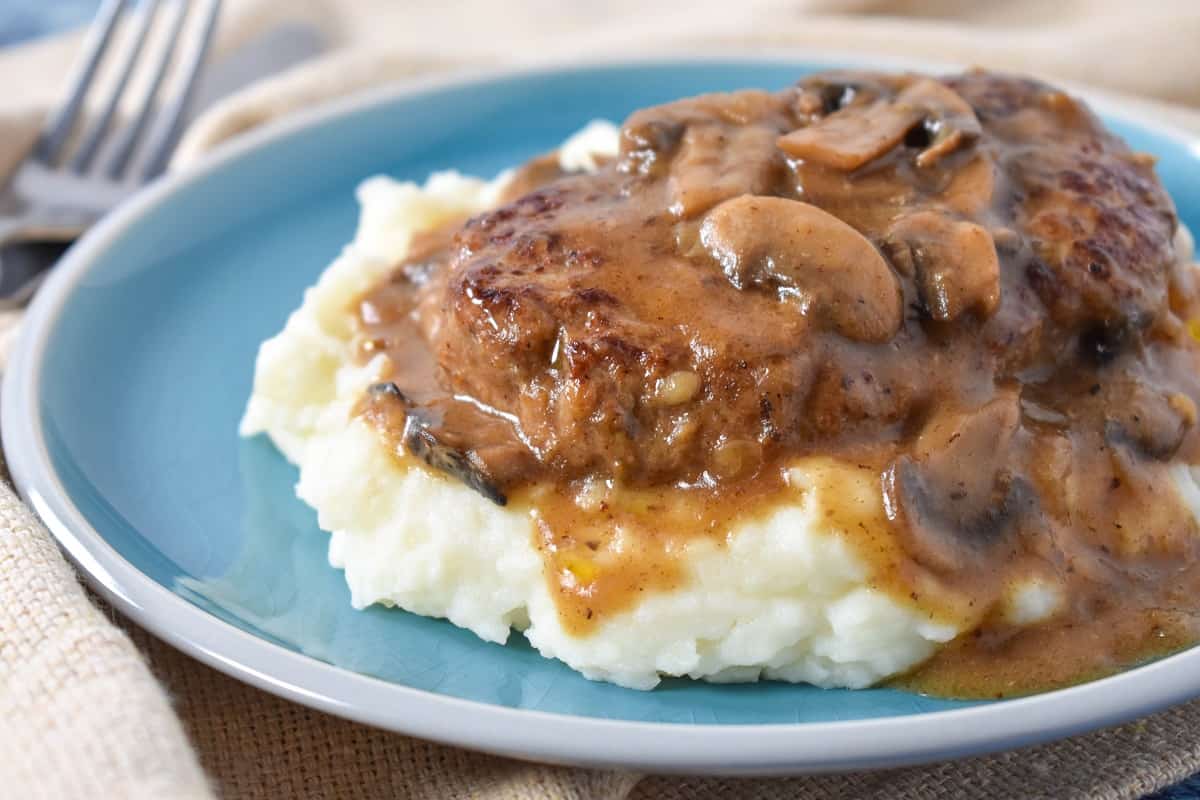 A close up of the finished dish served on a bed of mashed potatoes on a blue plate with a beige linen.