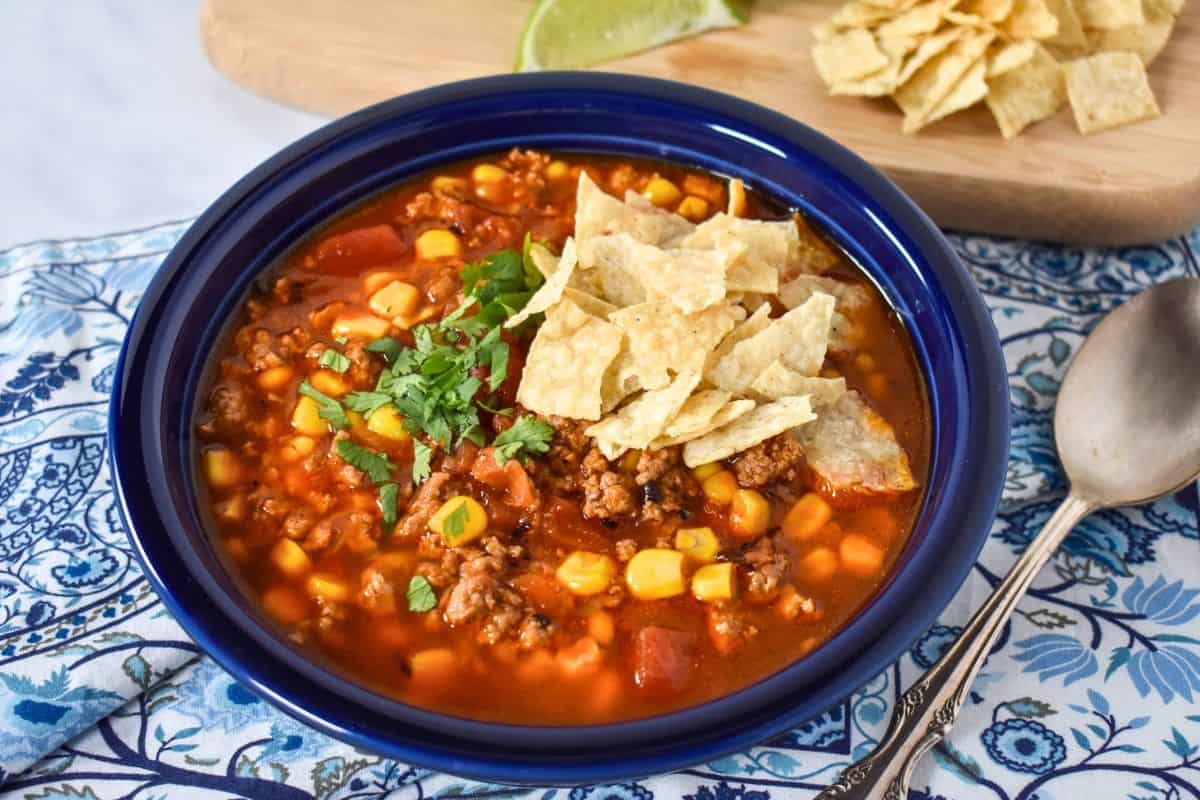 Ground turkey tortilla soup topped with crunchy tortilla chips and chopped cilantro, served in a blue bowl.