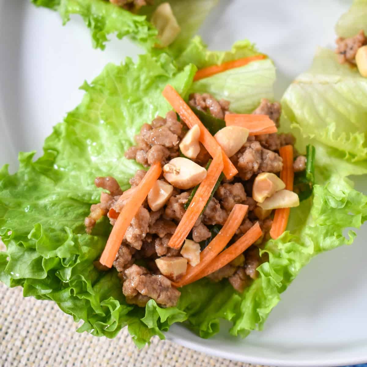 A pork lettuce wrap garnished with shredded carrots and peanuts, served on a white plate.