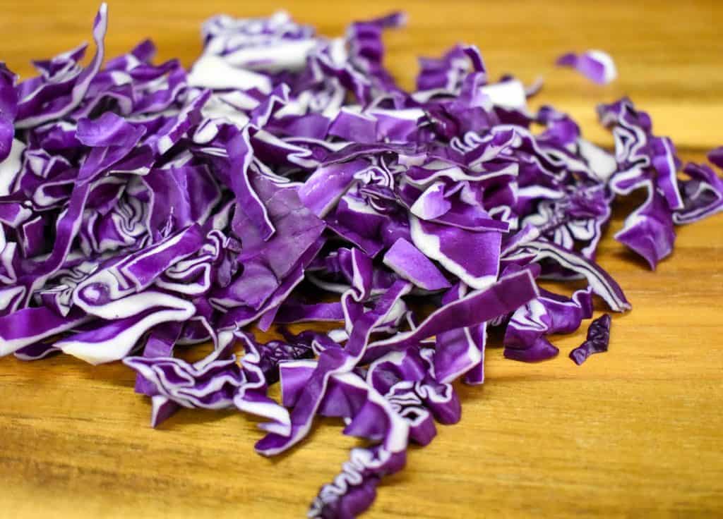 Shredded red cabbage on a wood cutting board.