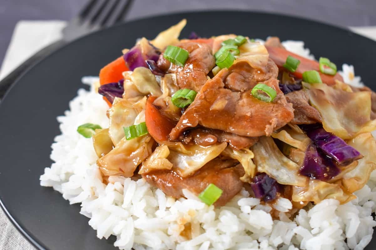 A close up of the finished dish served over white rice on a black plate.