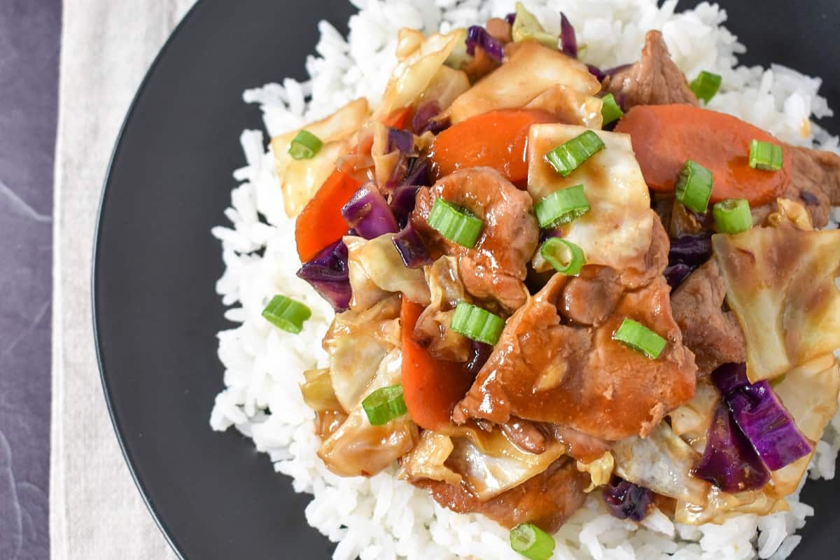 A close-up image of the pork stir fry served on a bed of white rice on a black plate.