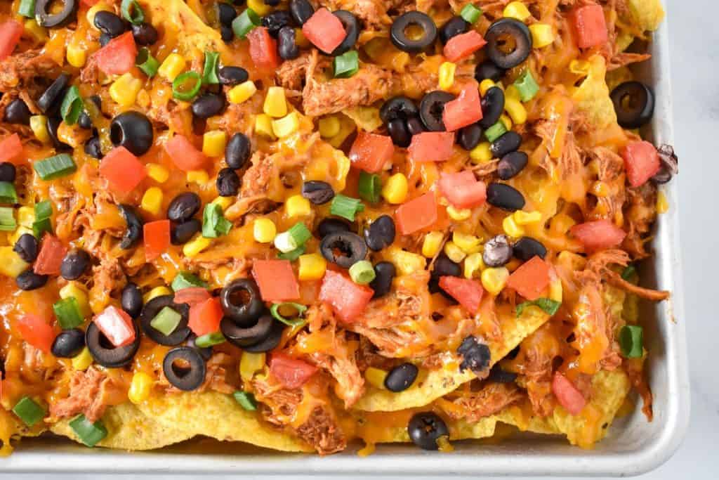 An image of the finished shredded chicken nachos on a sheet pan.