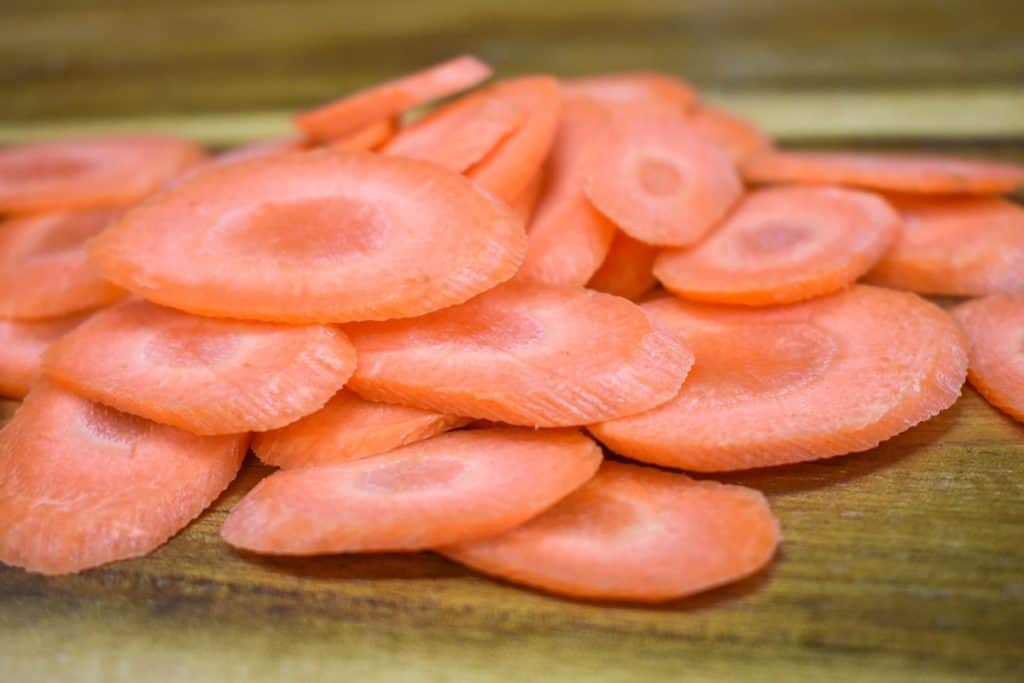 Carrots that are sliced thin and on the bias on a wood cutting board.