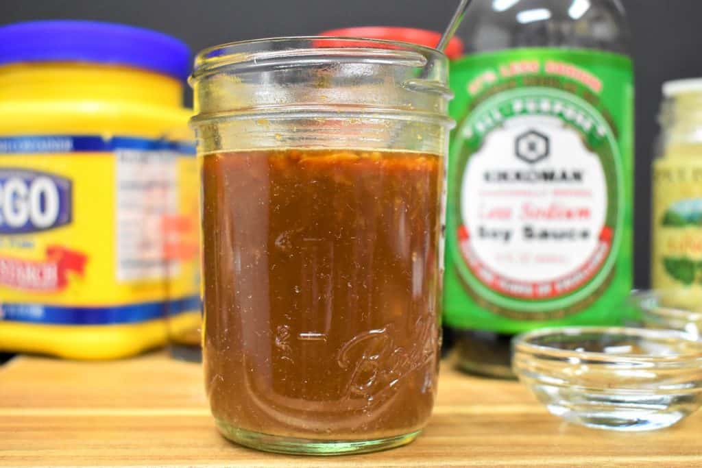 A small jar with the stir fry sauce. The ingredients for the sauce like the soy sauce and cornstarch are in the background.