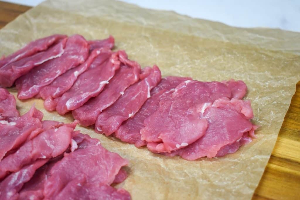 A pork tenderloin sliced thin and arranged on a piece of parchment paper.