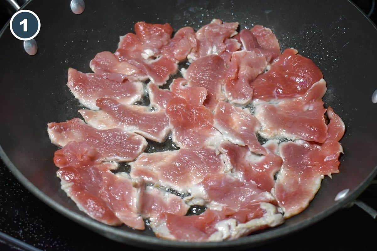 Thin slices of raw pork tenderloin cooking in oil in a large nonstick skillet.