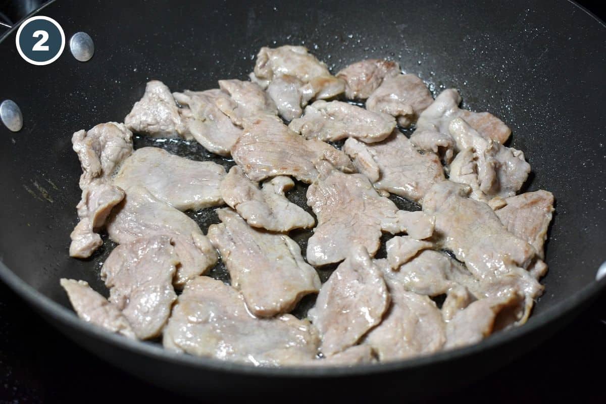 Pork tenderloin slices cooking in a skillet after being turned, with the meat beginning to brown.