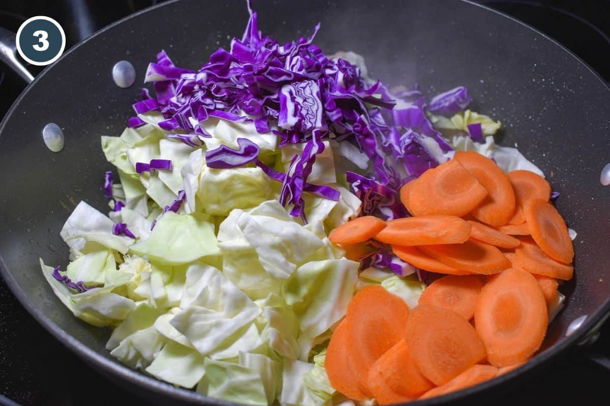 Chopped green cabbage, shredded red cabbage, and sliced carrots added to a skillet with cooked pork.