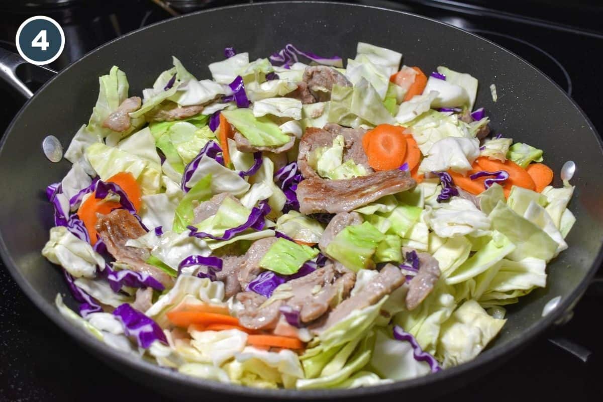 Pork tenderloin, green cabbage, red cabbage, and carrots stirred together in a large skillet.