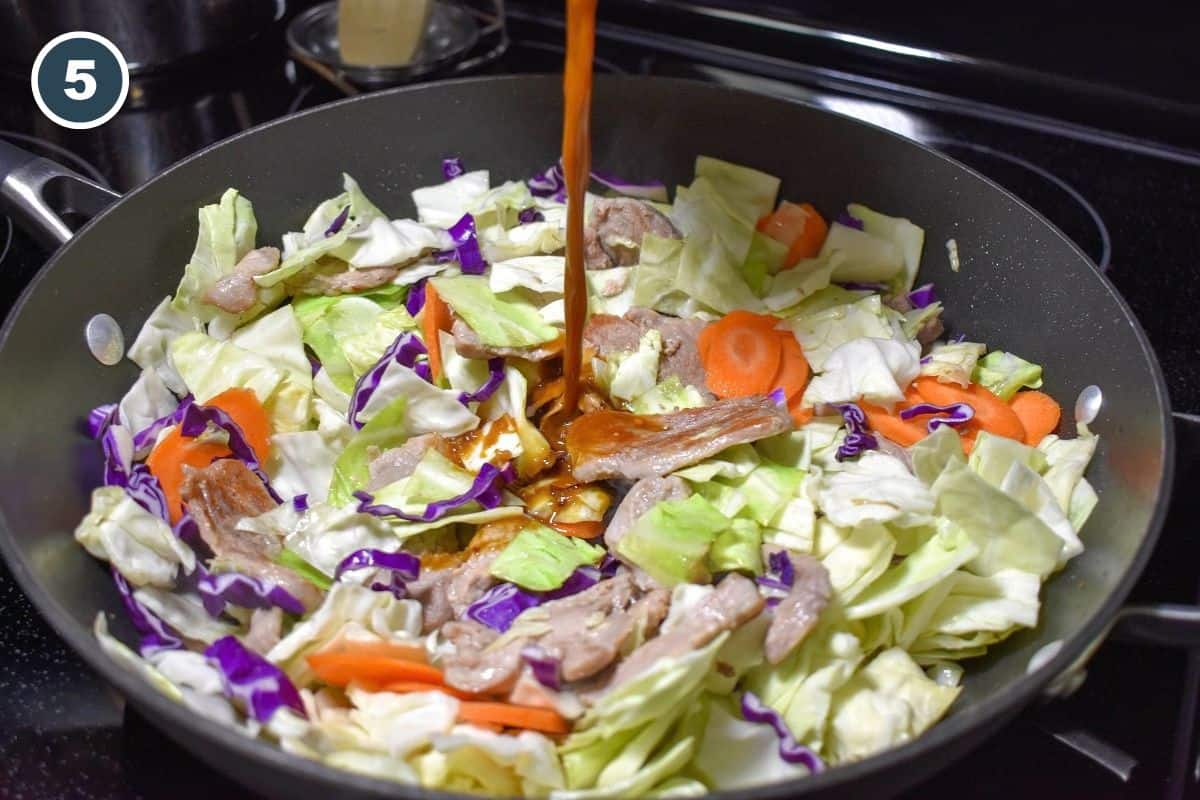 Homemade stir fry sauce being poured over pork tenderloin, cabbage, and carrots in a skillet.