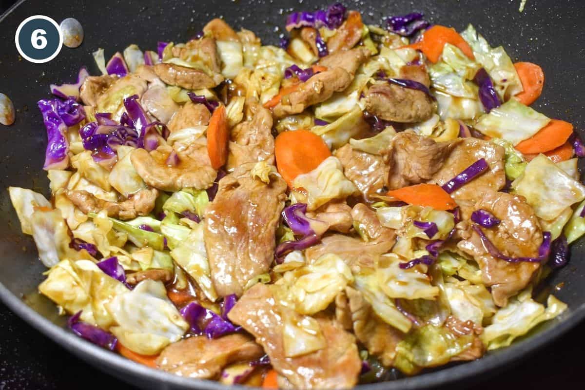 Finished pork and cabbage stir fry with carrots coated in a savory sauce in a skillet.