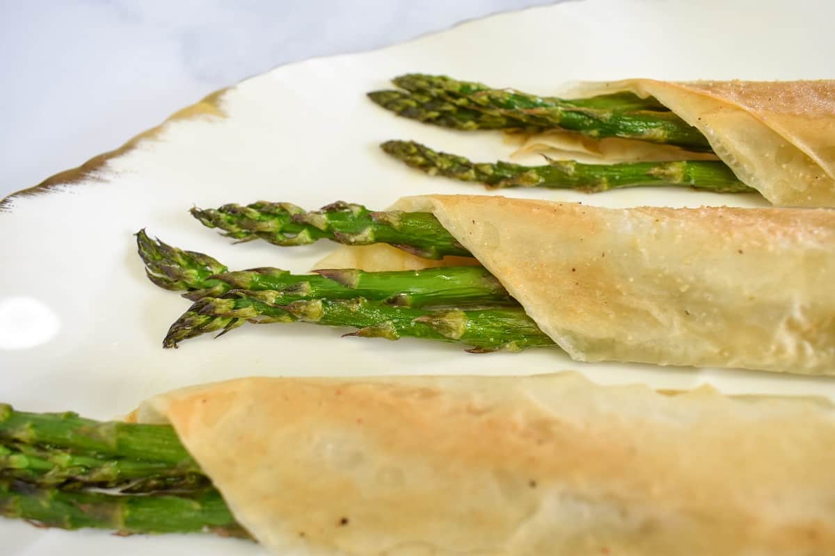 The finished asparagus rolls set on a white platters with gold trim.