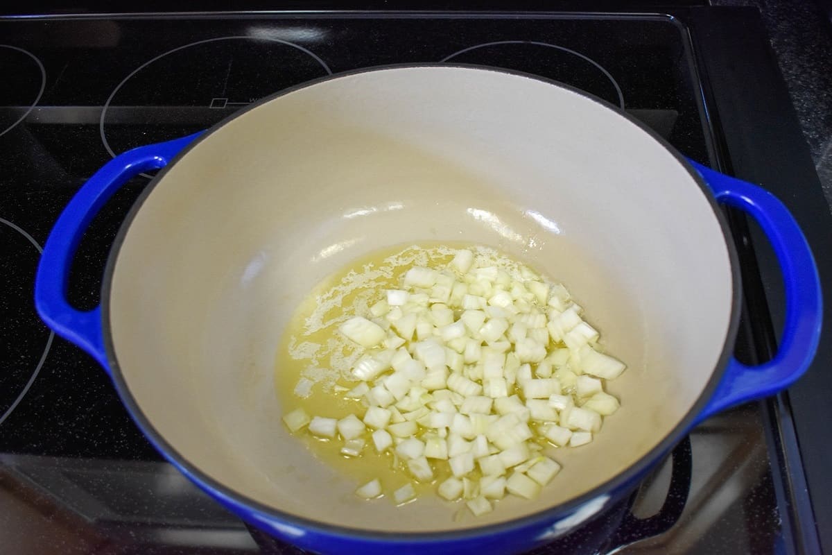Diced onions cooking in olive oil in a large blue and white pot.