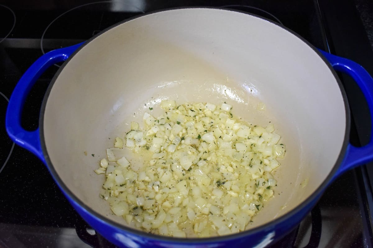 Diced onions, garlic, and herbs sautéing in a large blue and white pot.