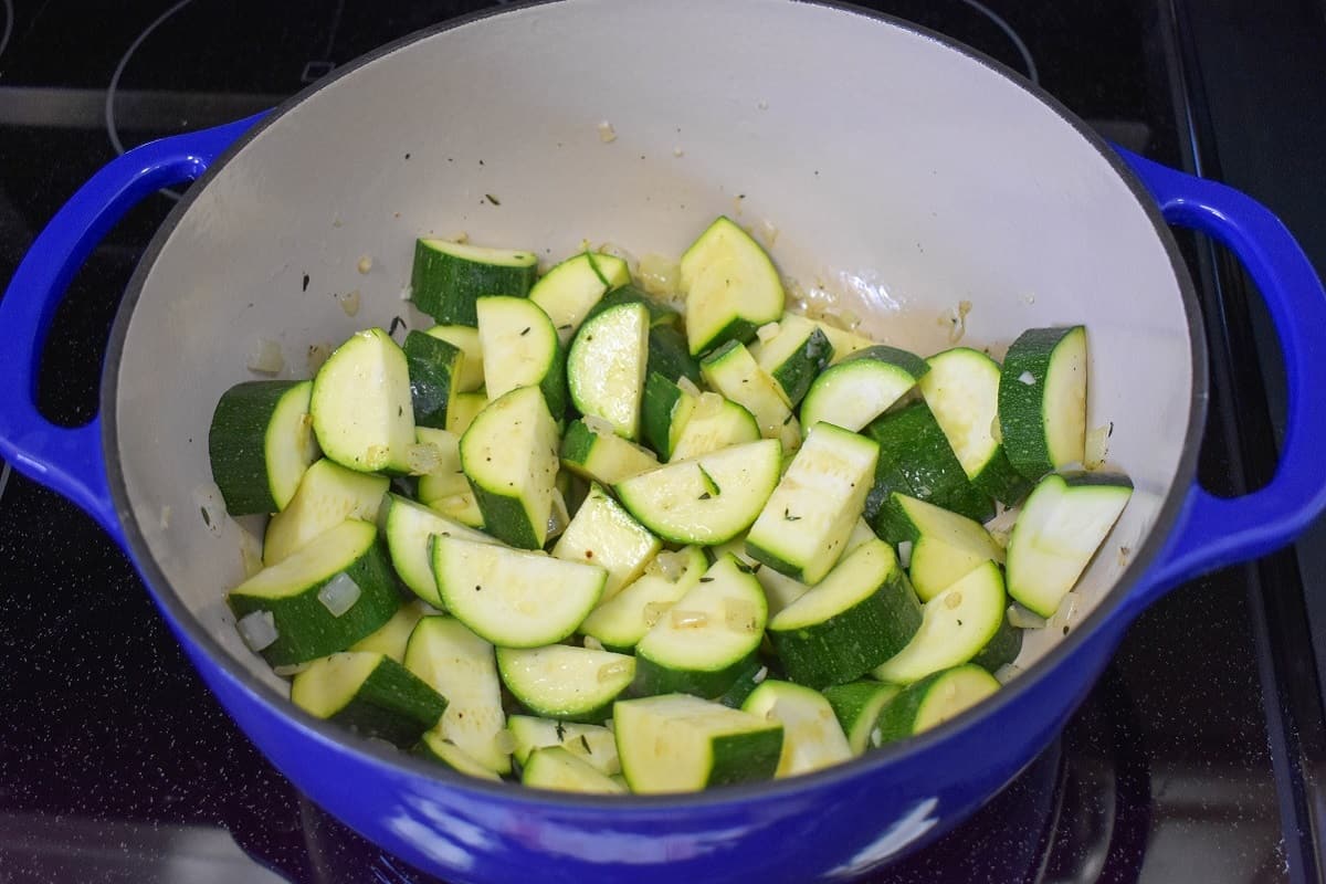 Cut zucchini , onions, and other spices sautéing in a large blue and white pot.