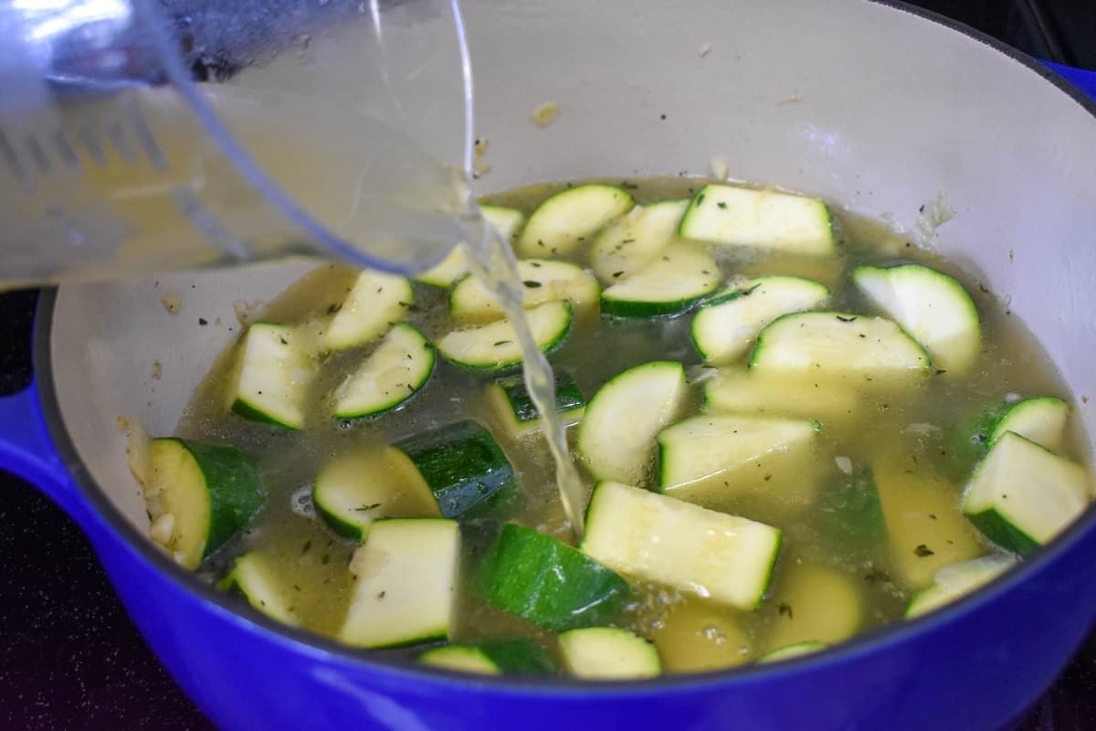 Broth being added to the zucchini and other ingredients in a large pot.