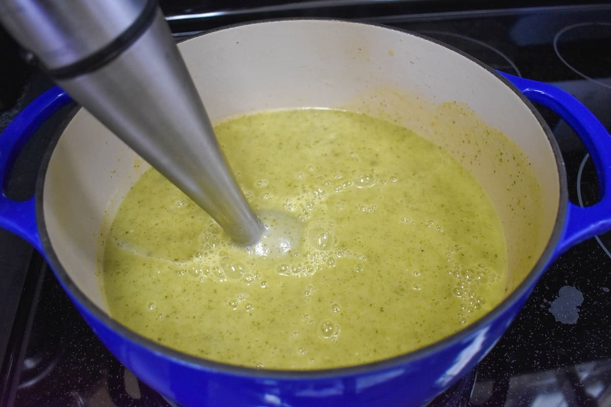 The soup being processed with an immersion blender in a blue and white pot.