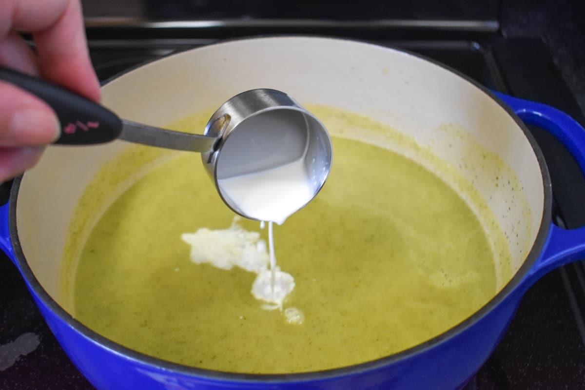 Cream being added to the processed zucchini soup in a large blue and white pot.