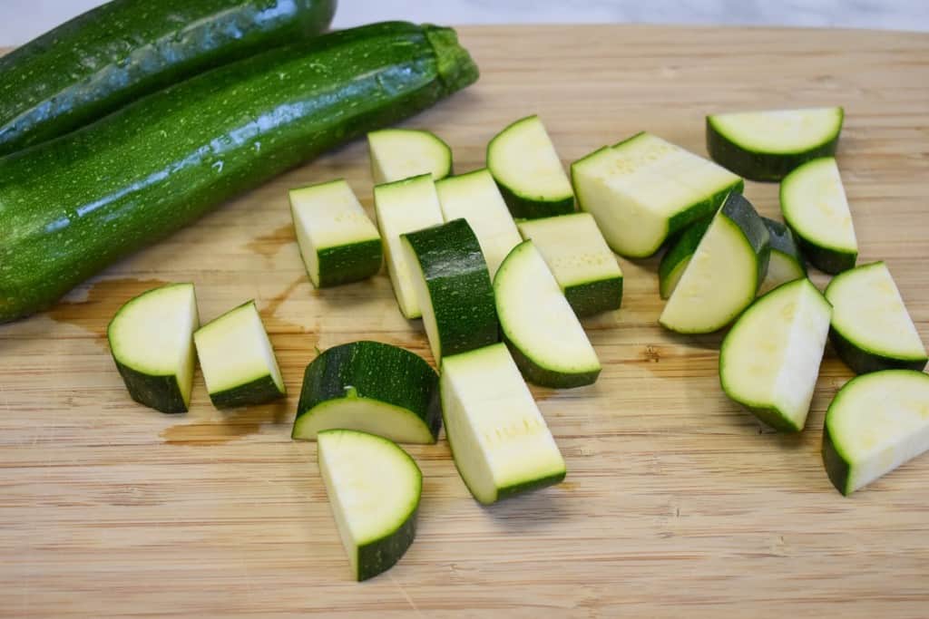 Zucchini on a cutting board with one cut into roughly one inch pieces.