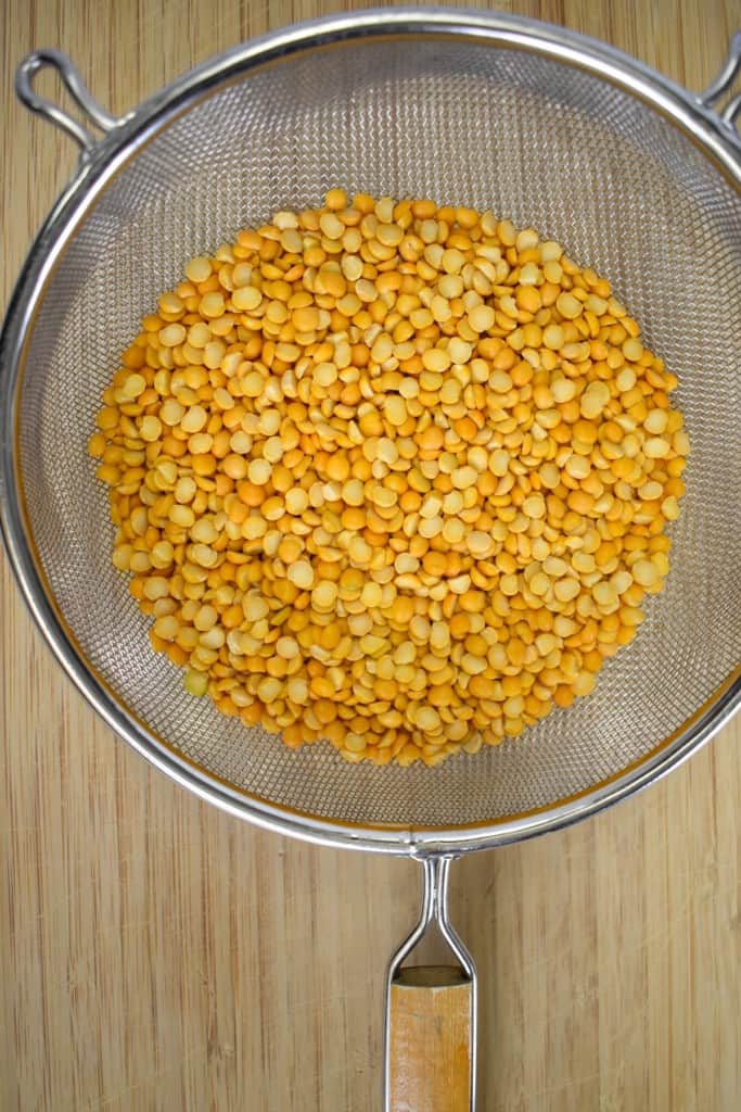 Yellow split peas in a large mesh strainer set on a wood cutting board.