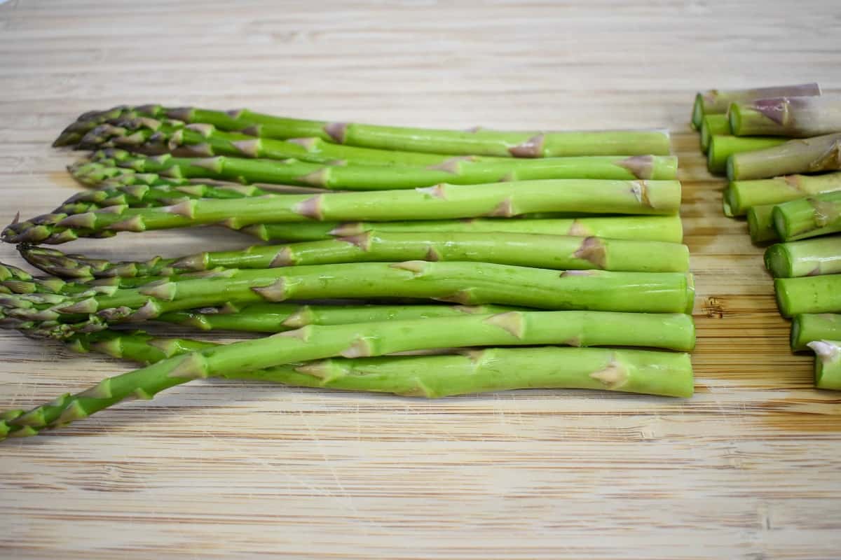 Asparagus with the ends trimmed off on a wood cutting board.