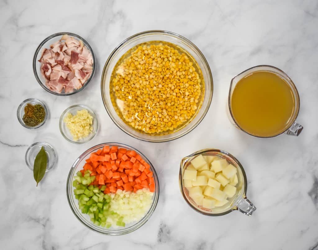 The prepped ingredients for the soup separated in clear containers and arranged on a white table.